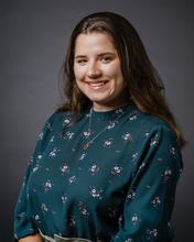 A young woman with brunette hair wears a cool patterned blouse